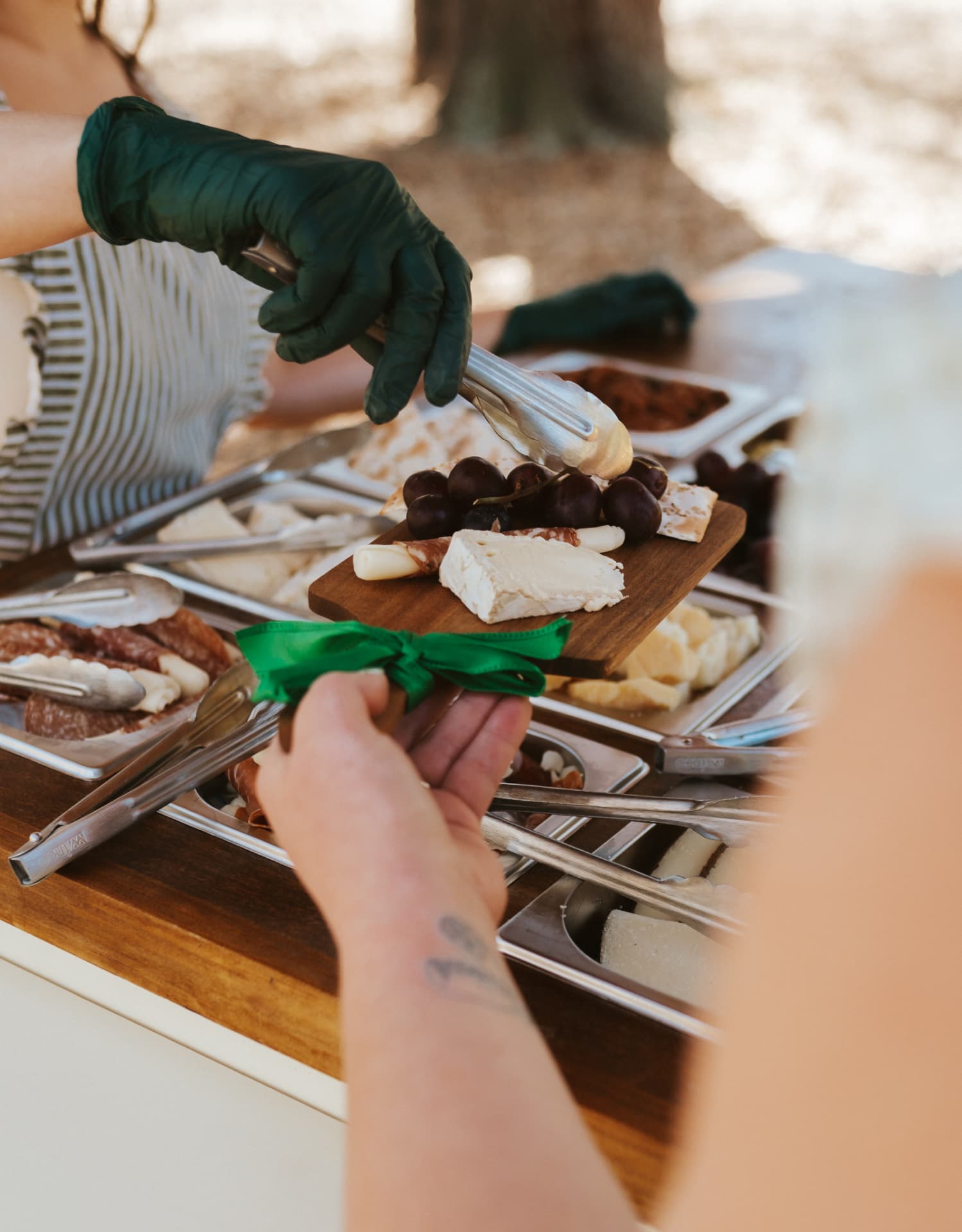 An attendant adding grapes to a guest's wooden charcuterie board