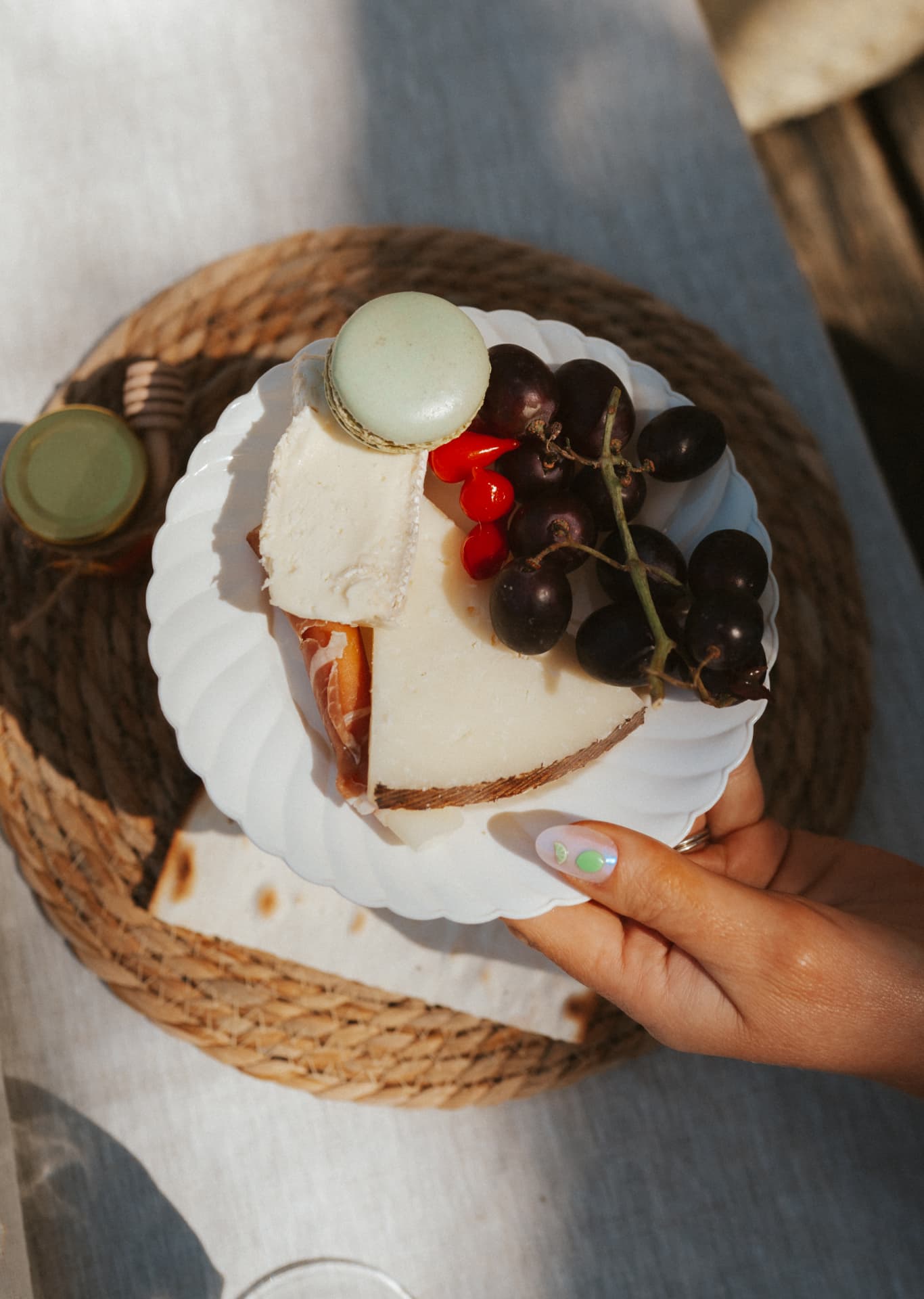 A guest holding a plate of cheese, grapes, peppers and a pistachio macaron